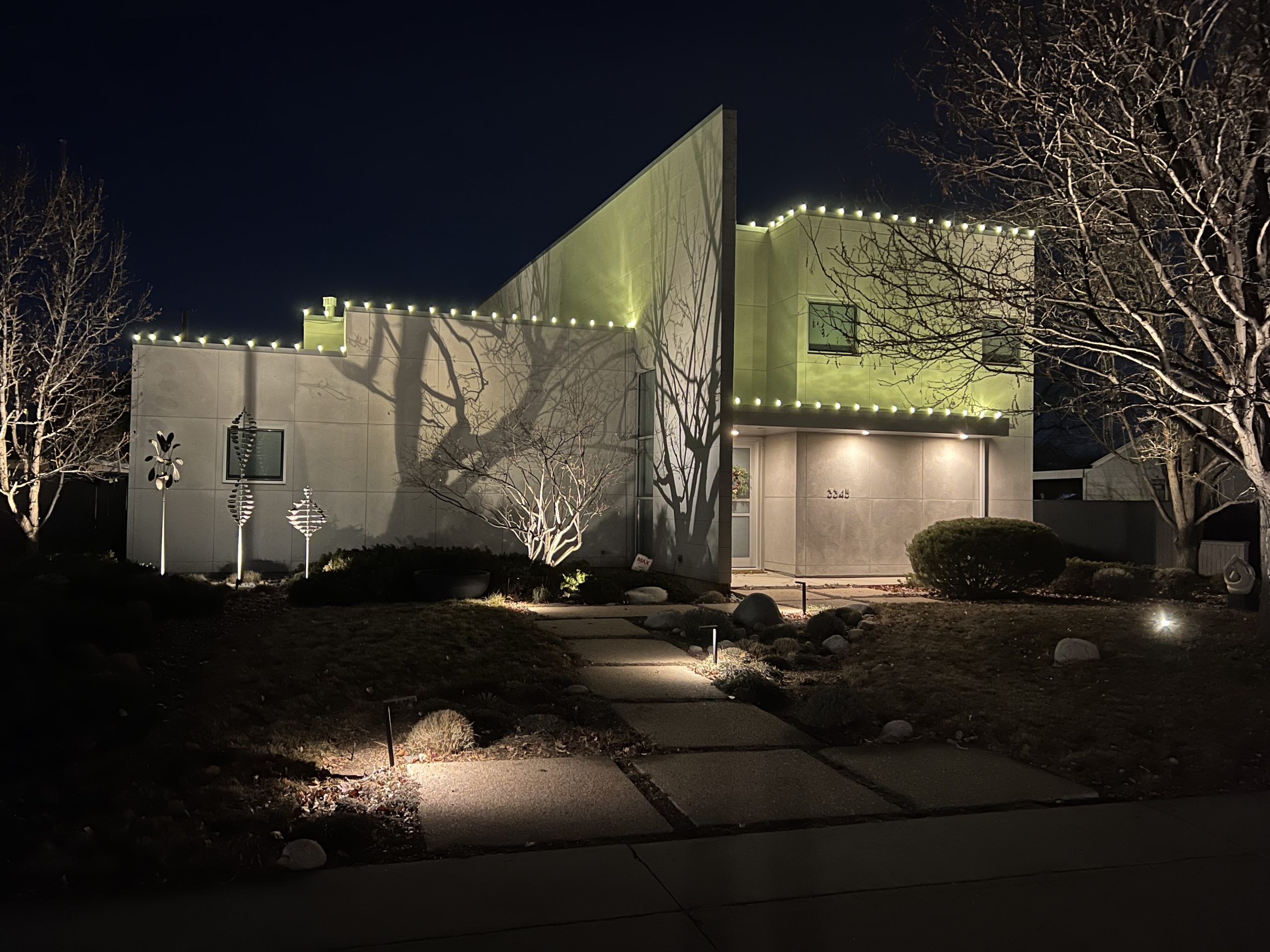 A modern house is illuminated at night with festive lights and dramatic shadows