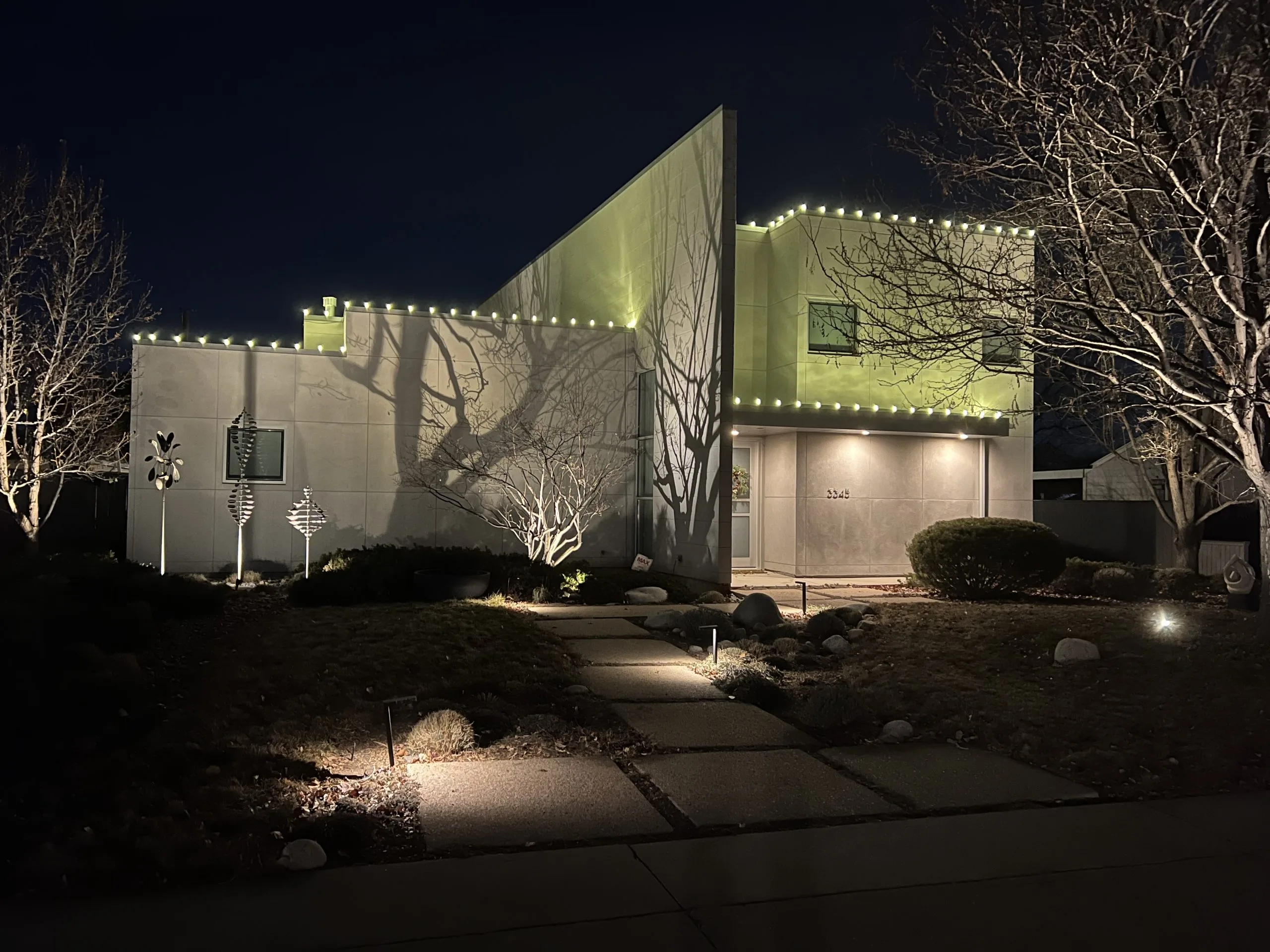A modern house is illuminated at night with festive lights and dramatic shadows