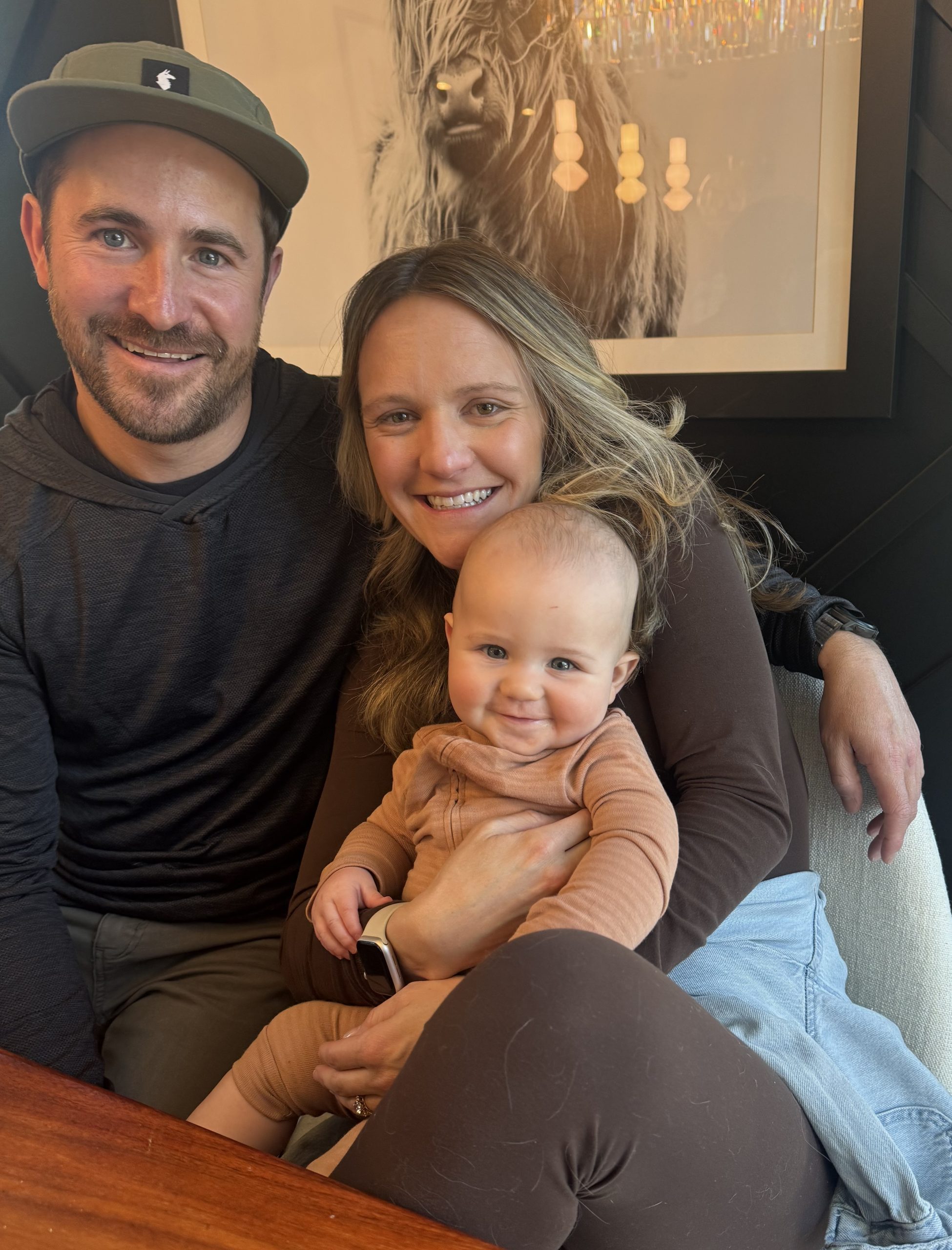 A smiling couple holds a joyful baby in a cozy indoor setting