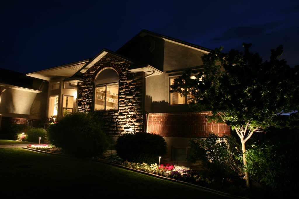 A well-lit house stands in a beautifully landscaped yard at night