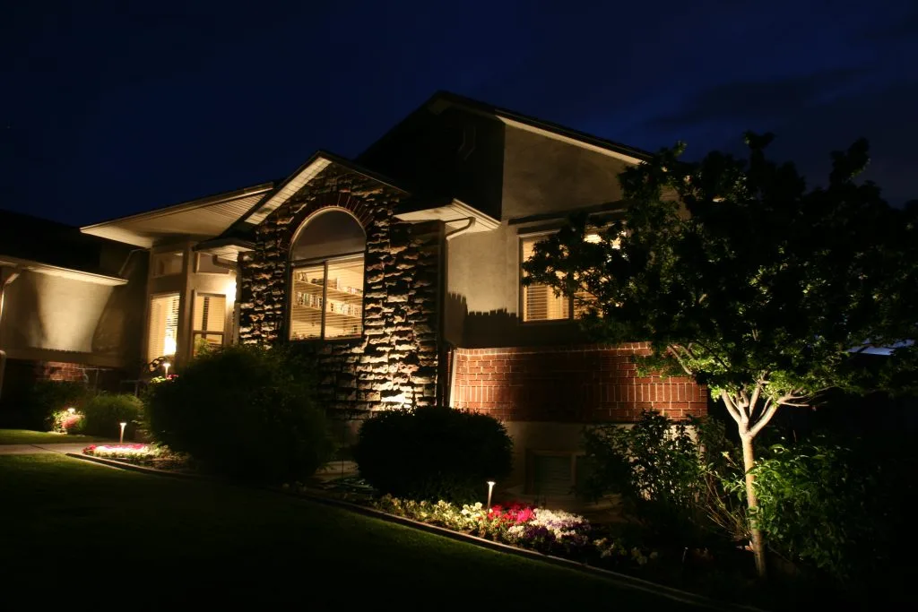 A well-lit house stands in a beautifully landscaped yard at night