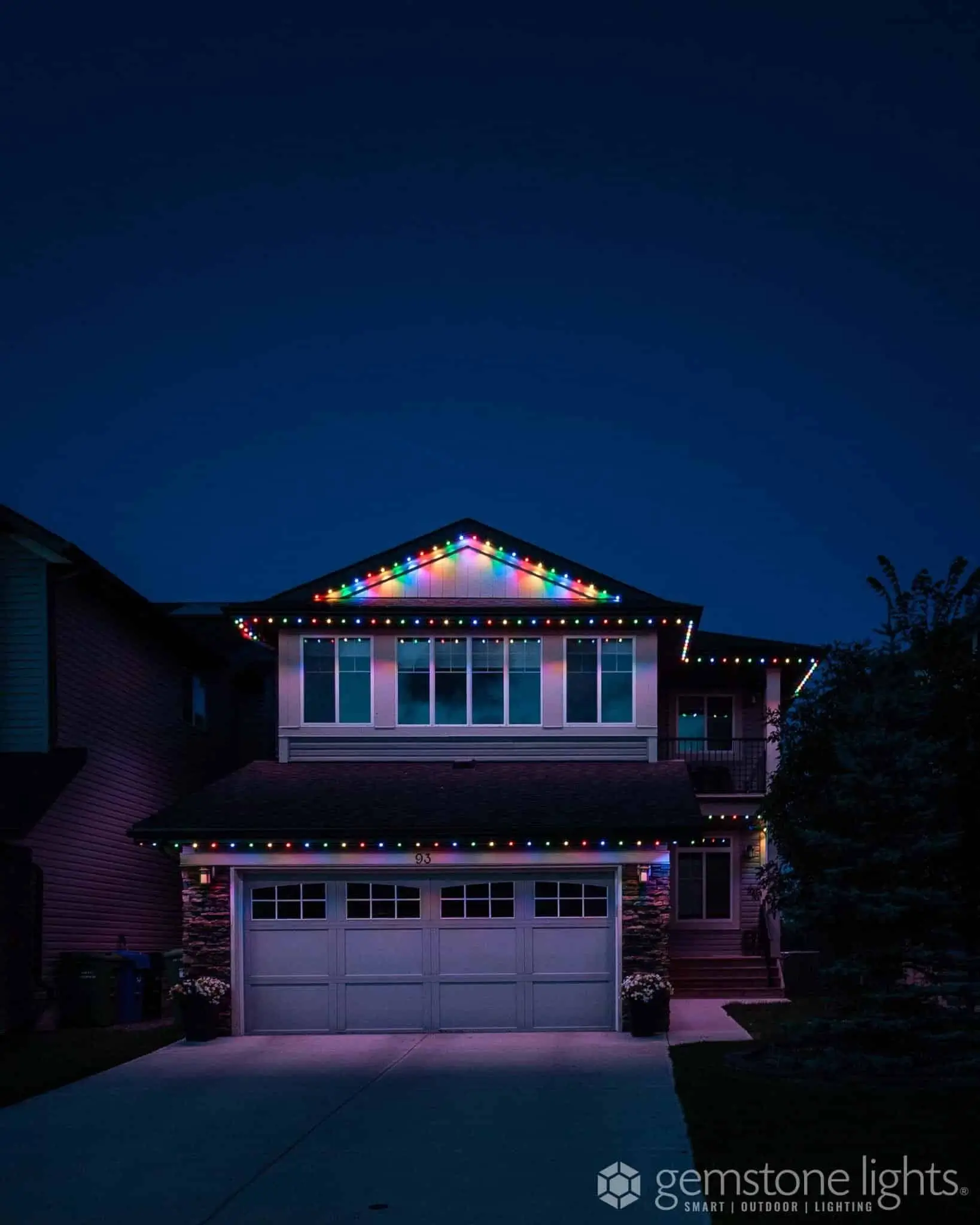 A house is illuminated with colorful lights along the roofline against a twilight sky