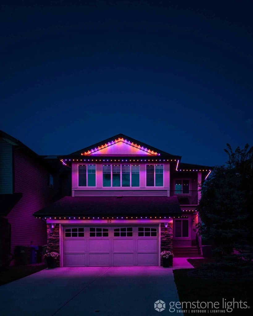 A house is illuminated with vibrant purple and orange lights against a nighttime sky