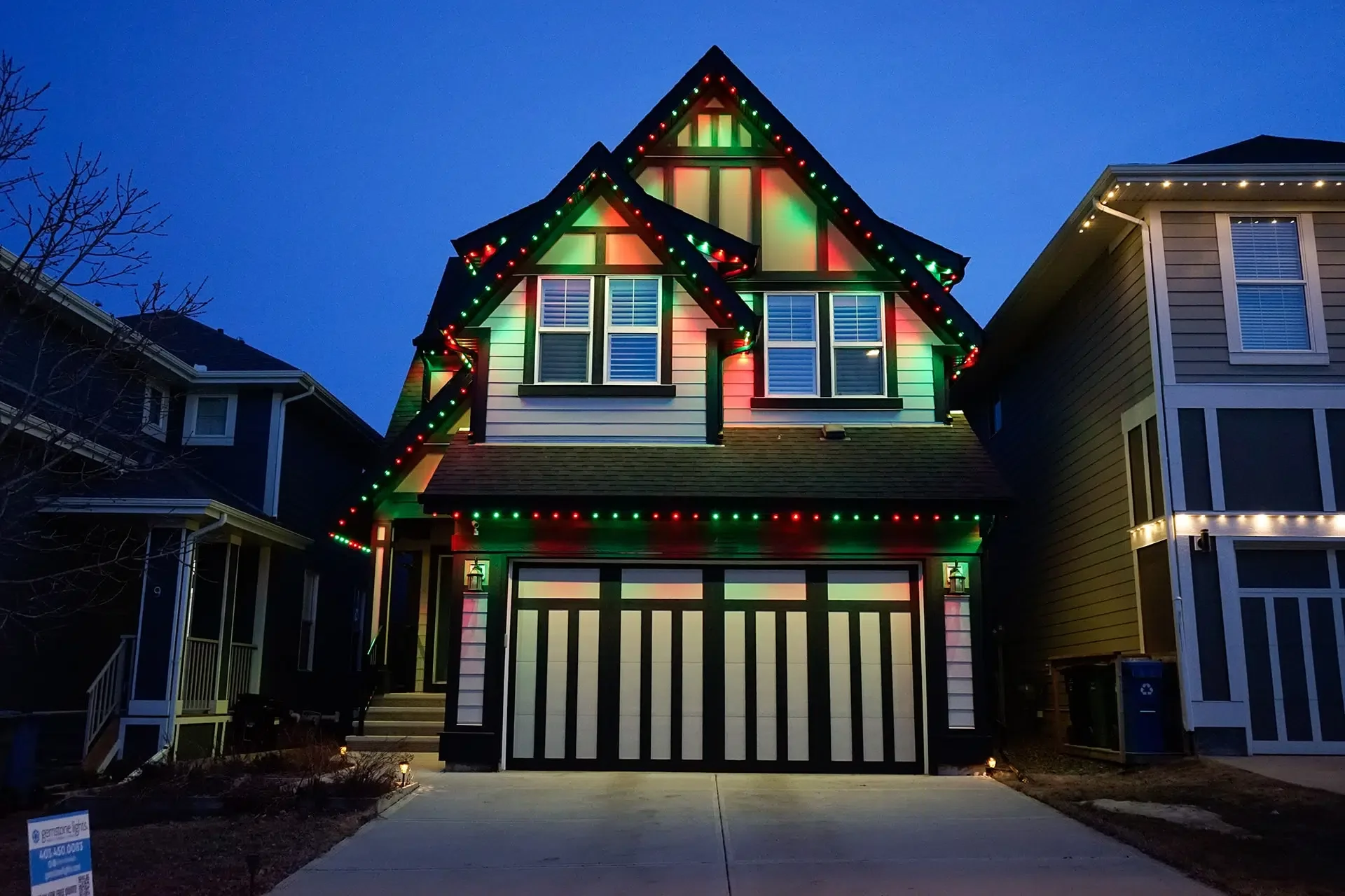 A house adorned with colorful holiday lights glows warmly against a twilight sky