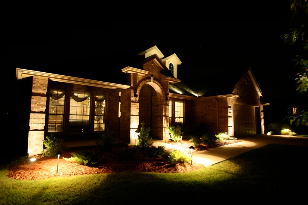 A well-lit, welcoming house stands prominently at night, surrounded by soft landscaping