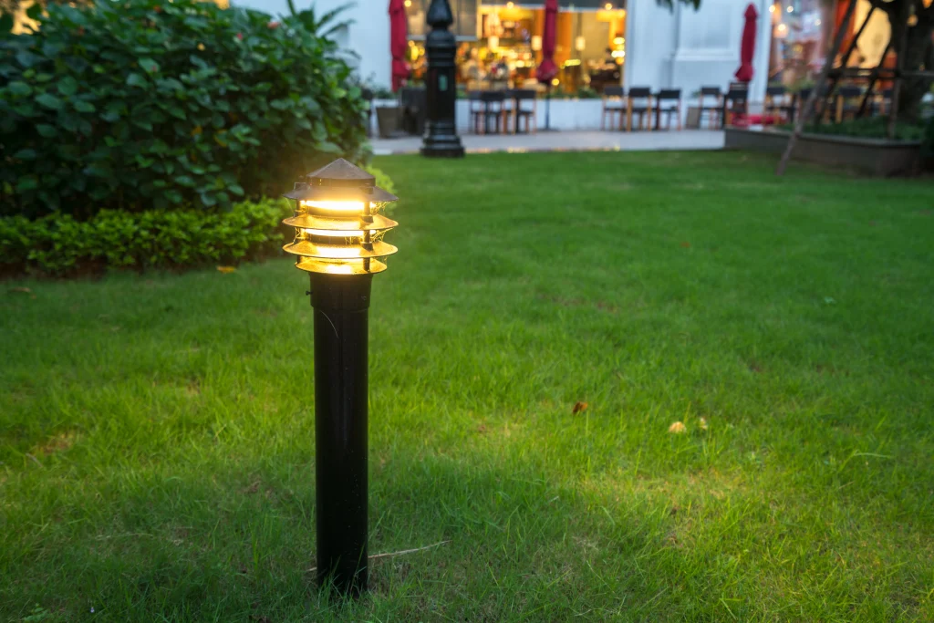 A decorative garden light illuminates a lush, green lawn in the evening