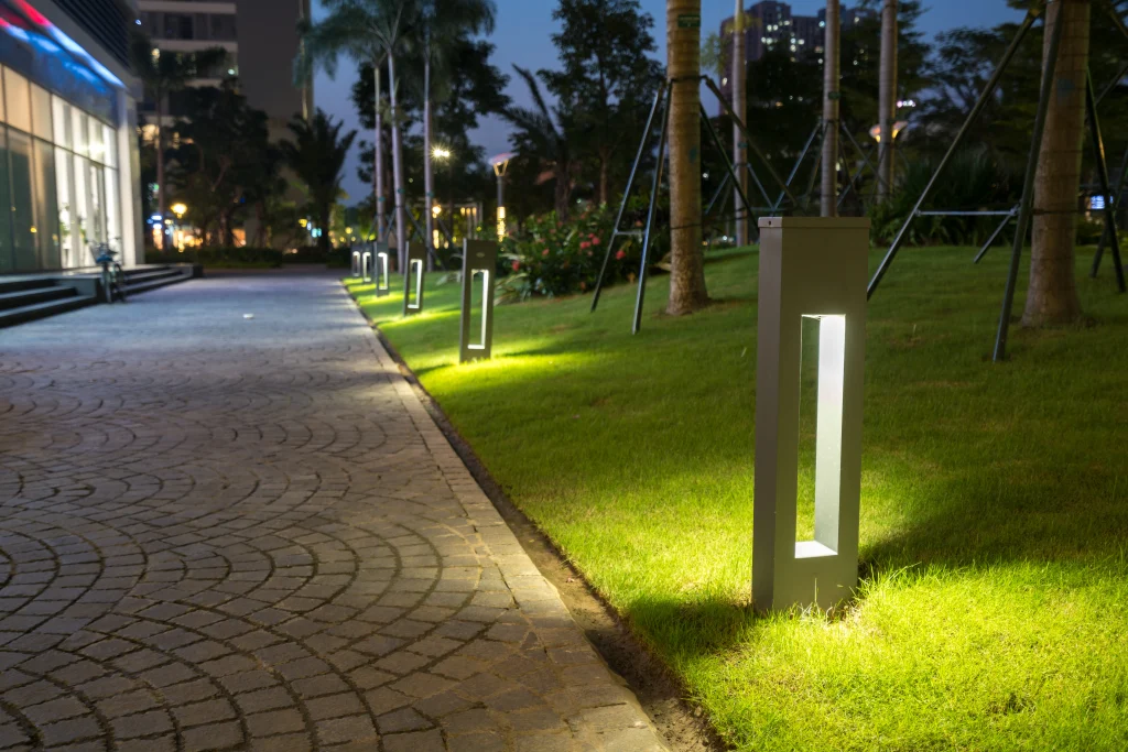 Pathway lined with modern, illuminated lamp posts amidst lush green grass at night