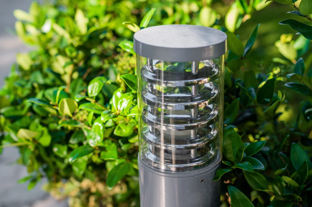 A sleek, circular light fixture stands amidst lush green foliage