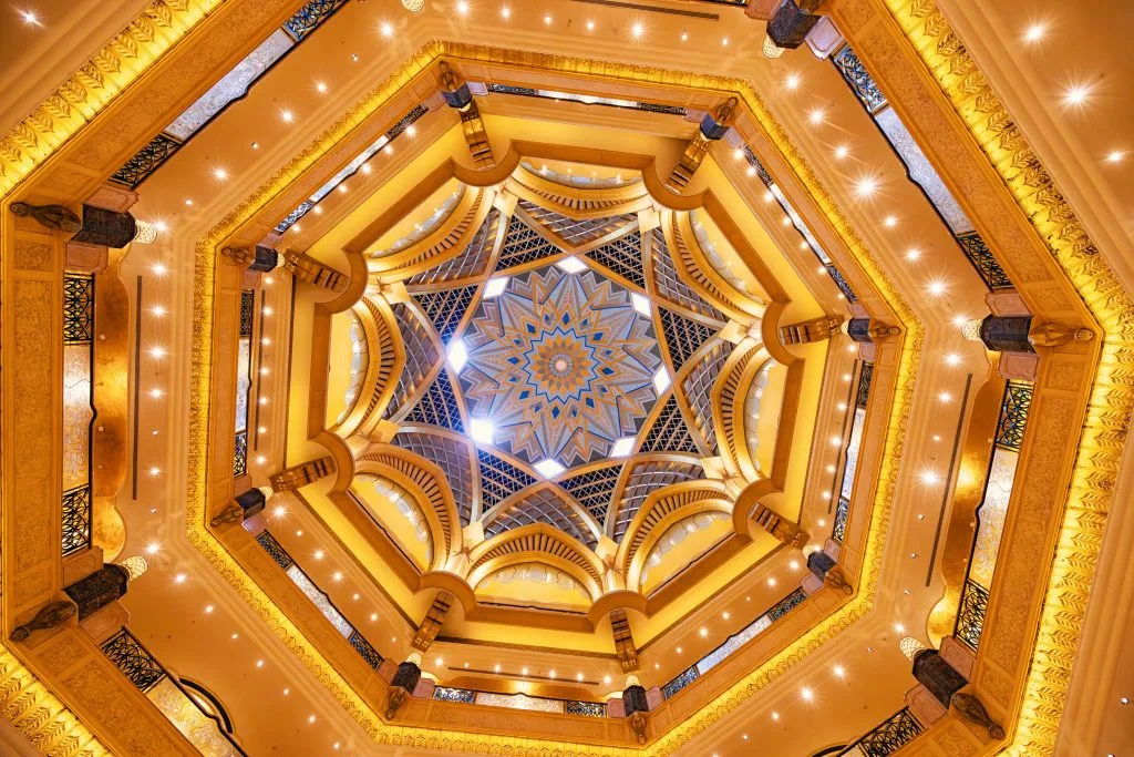 A grand, ornate ceiling features intricate patterns and warm golden lighting