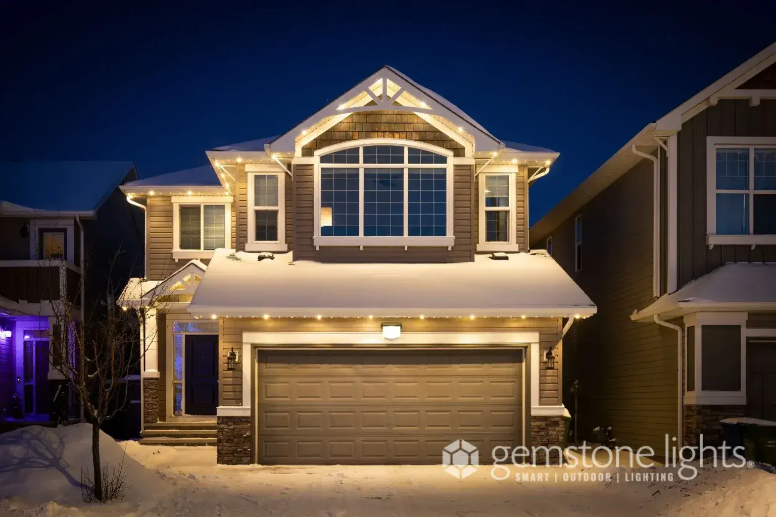 A well-lit house in a snowy neighborhood exudes warmth during twilight