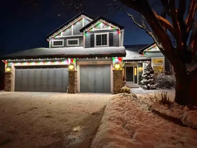 A snow-covered house is adorned with colorful holiday lights at night