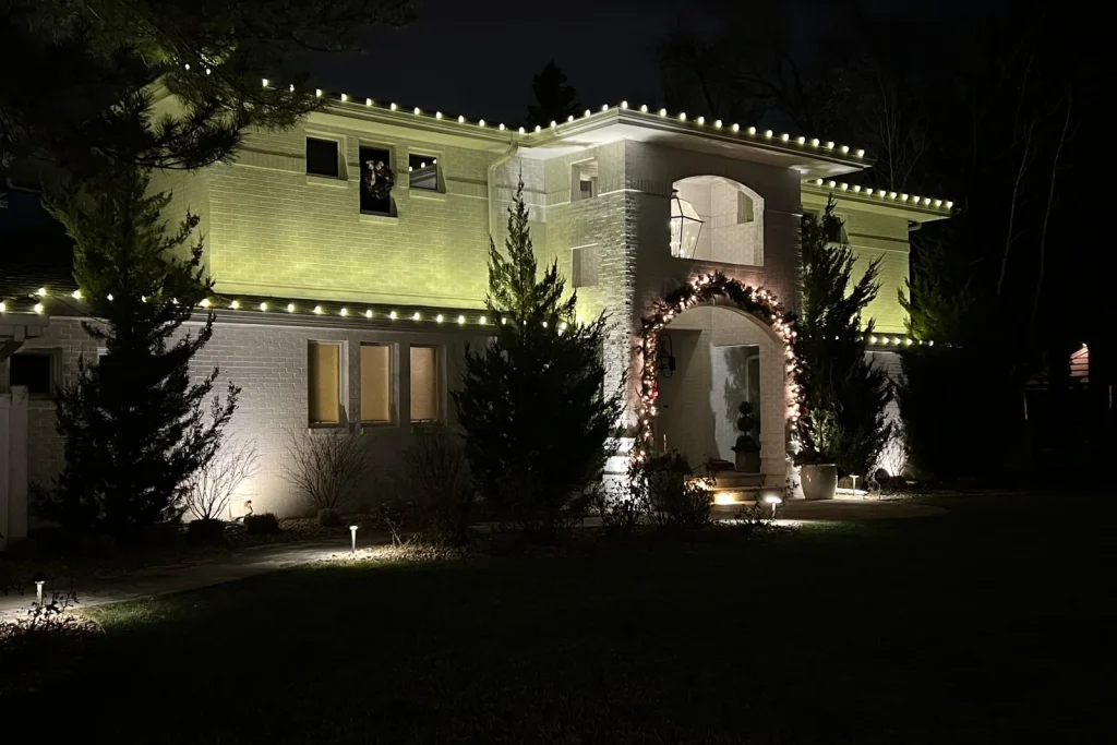 White home with warm white roofline lighting and a lit entry arch